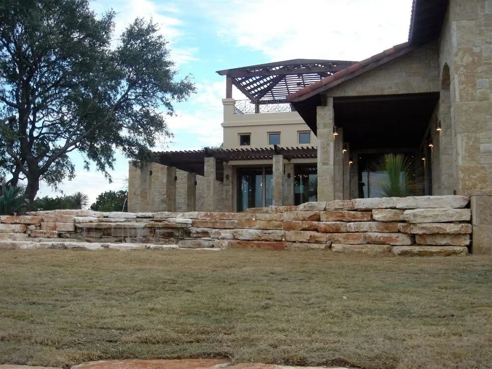 Stone Hill Country lodge with a timber pergola above tiered limestone retaining walls and lawn
