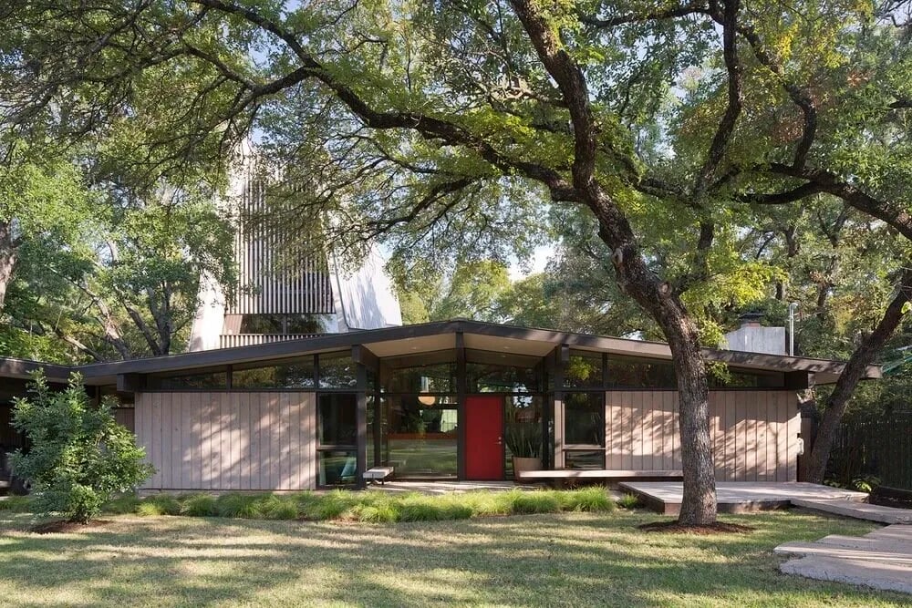 Low-slung midcentury home with a red front door tucked among oak trees
