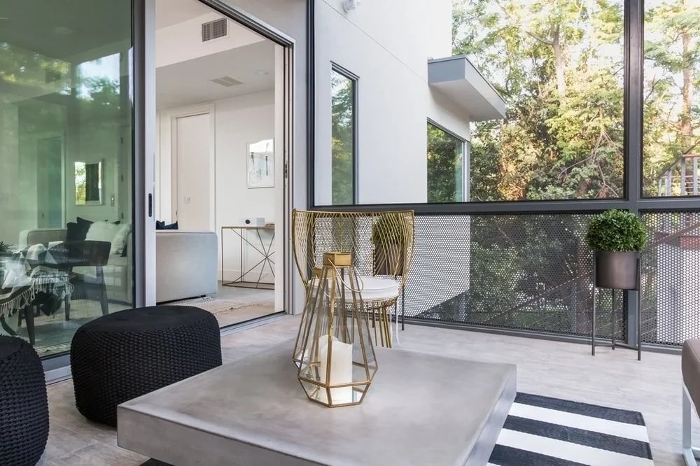 Covered patio with concrete-top table, looking through glass walls into a bright open kitchen