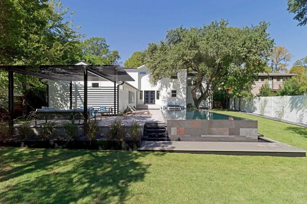 Aerial of a dark geometric pool with a spillway spa and stepped deck beside a white modern home