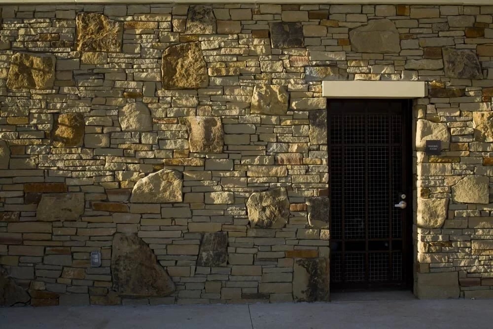Rough stone masonry wall with a dark steel door, lit in warm low-angle light