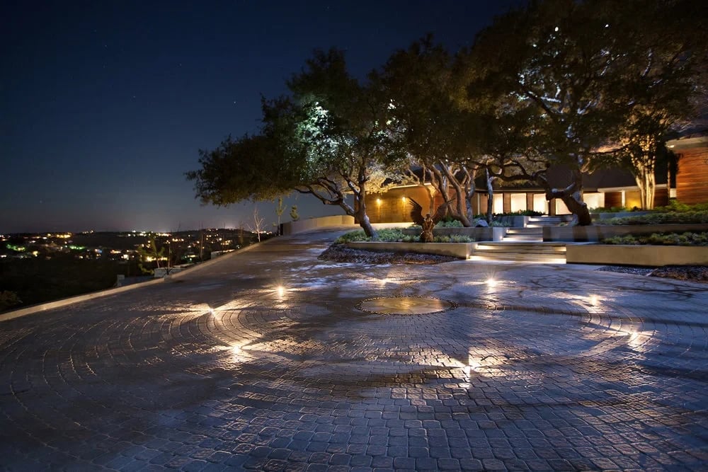 Lit stone deck under live oaks at night, overlooking distant city lights across the Hill Country