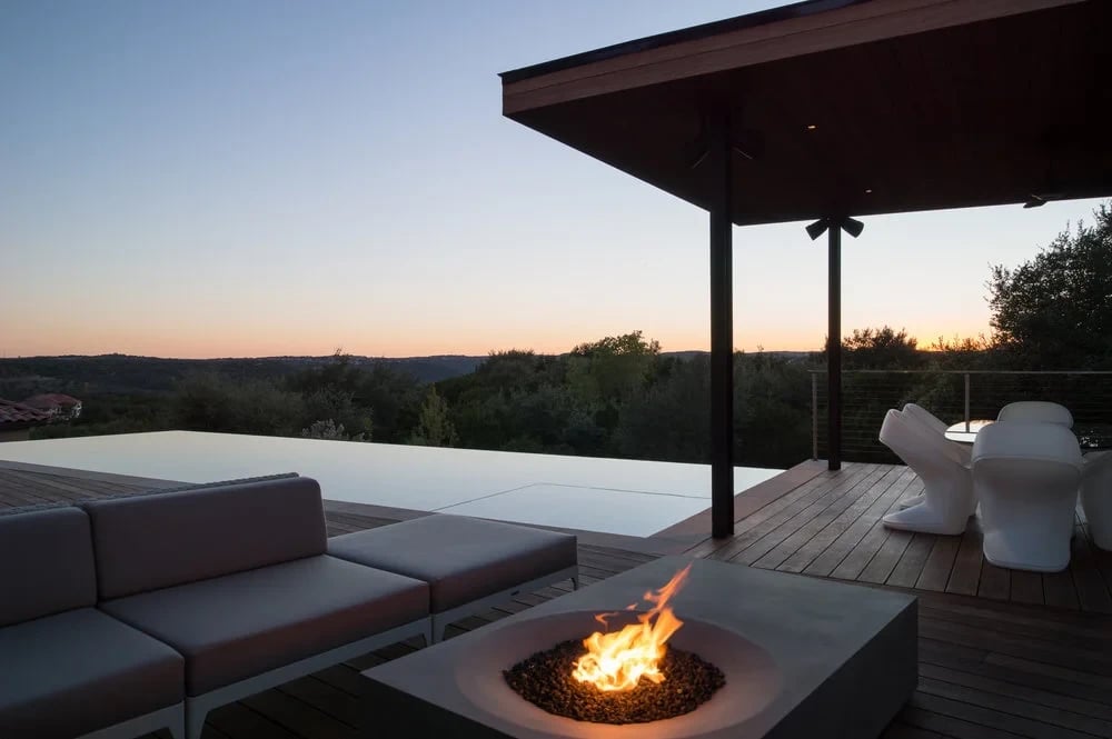 Covered deck with a concrete fire pit and lounge sofa overlooking the Hill Country at sunset