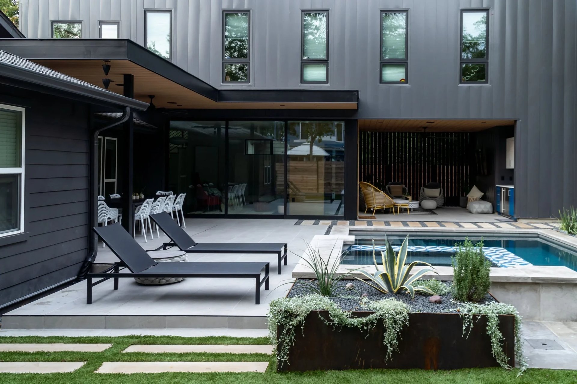 Black modern home with lounge chairs, a corten planter, and a tiled pool in the backyard