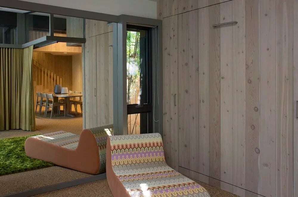 Cedar-paneled room with patterned lounge chairs and a glass door opening to a dining area and garden