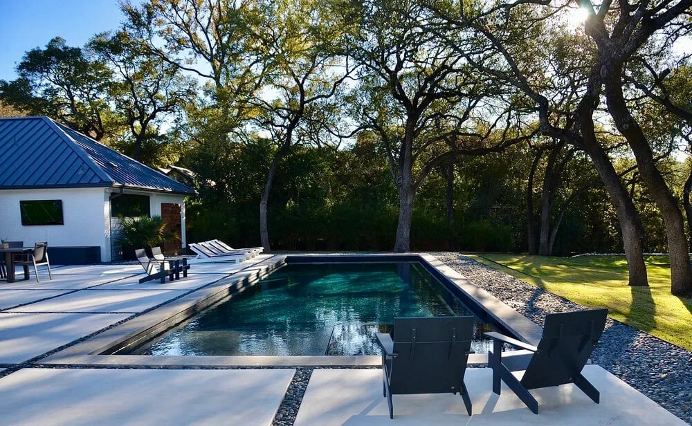 Geometric pool with lounge chairs beside a white home, framed by oaks in West Lake Hills