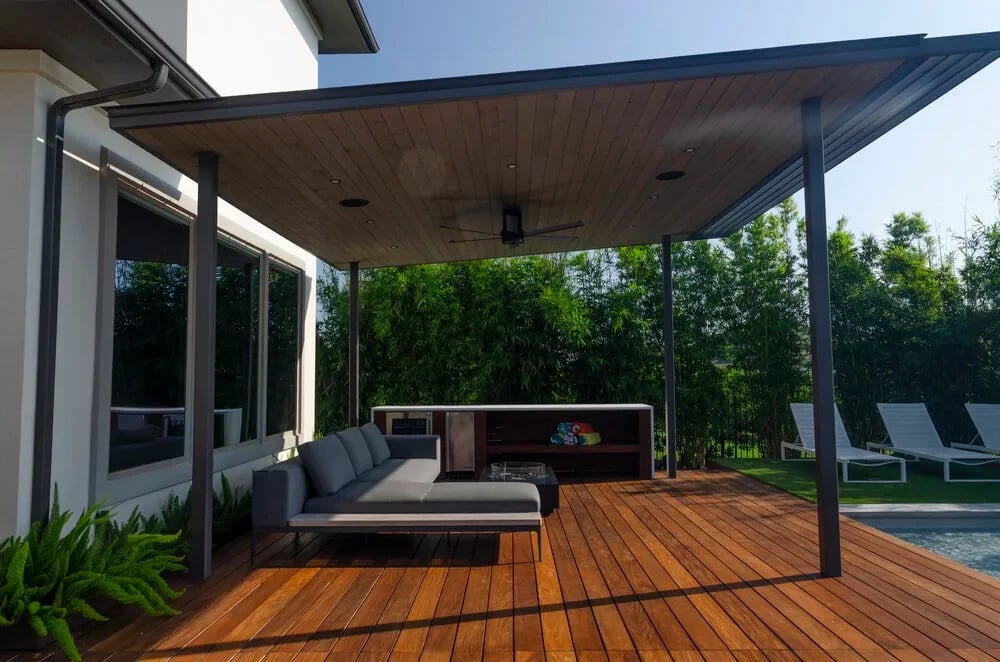 Covered ipe deck with a sofa and outdoor kitchen beside a geometric pool screened by bamboo
