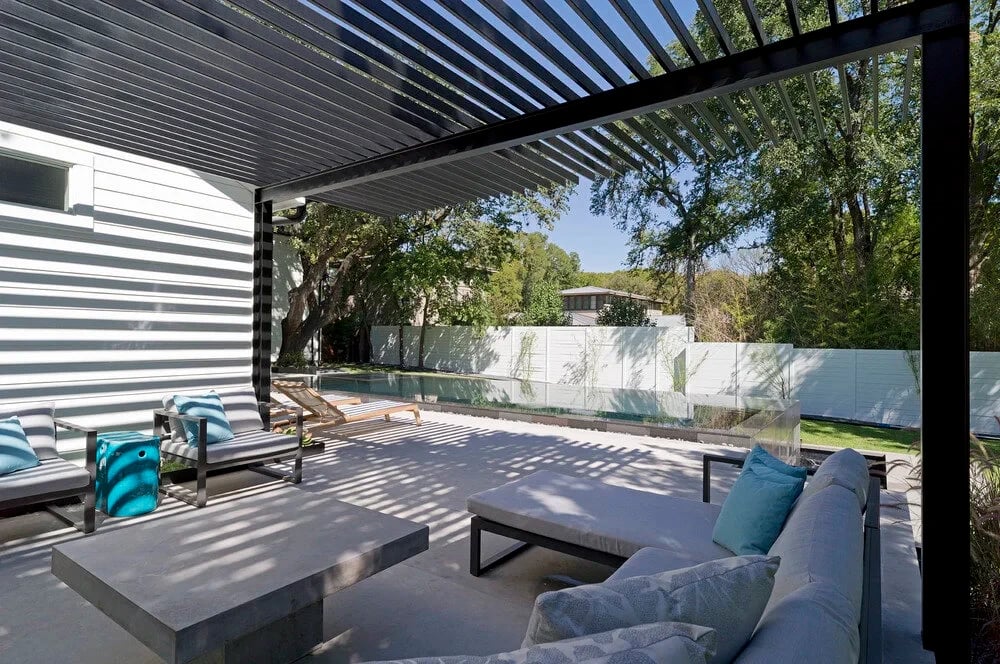 Covered patio with louvered steel pergola, lounge seating and turquoise accents beside a glass-edged pool