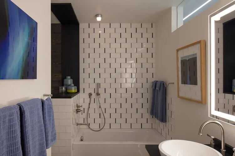 Modern bathroom with white subway-tile tub surround, a backlit mirror and blue towels