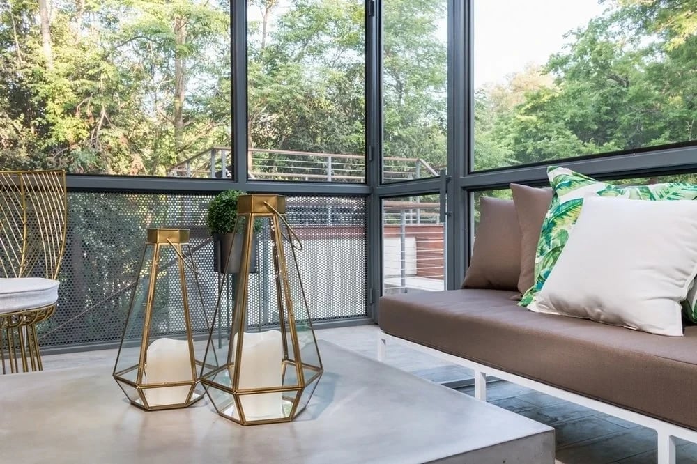 Sunroom corner with a cushioned bench and geometric brass planter beside floor-to-ceiling windows