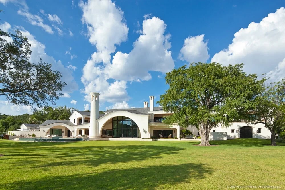 Sprawling white-stone estate with curved roofs and a round tower across a wide green lawn