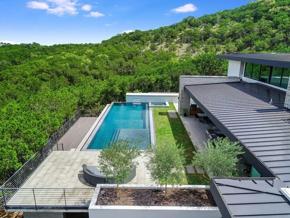 Aerial of a modern home with a lap-style infinity pool and terraces set into wooded hillside