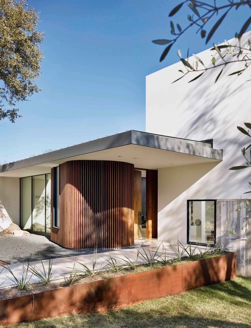 Modern home with a curved wood entry, flat roof, and agave plantings under a clear sky