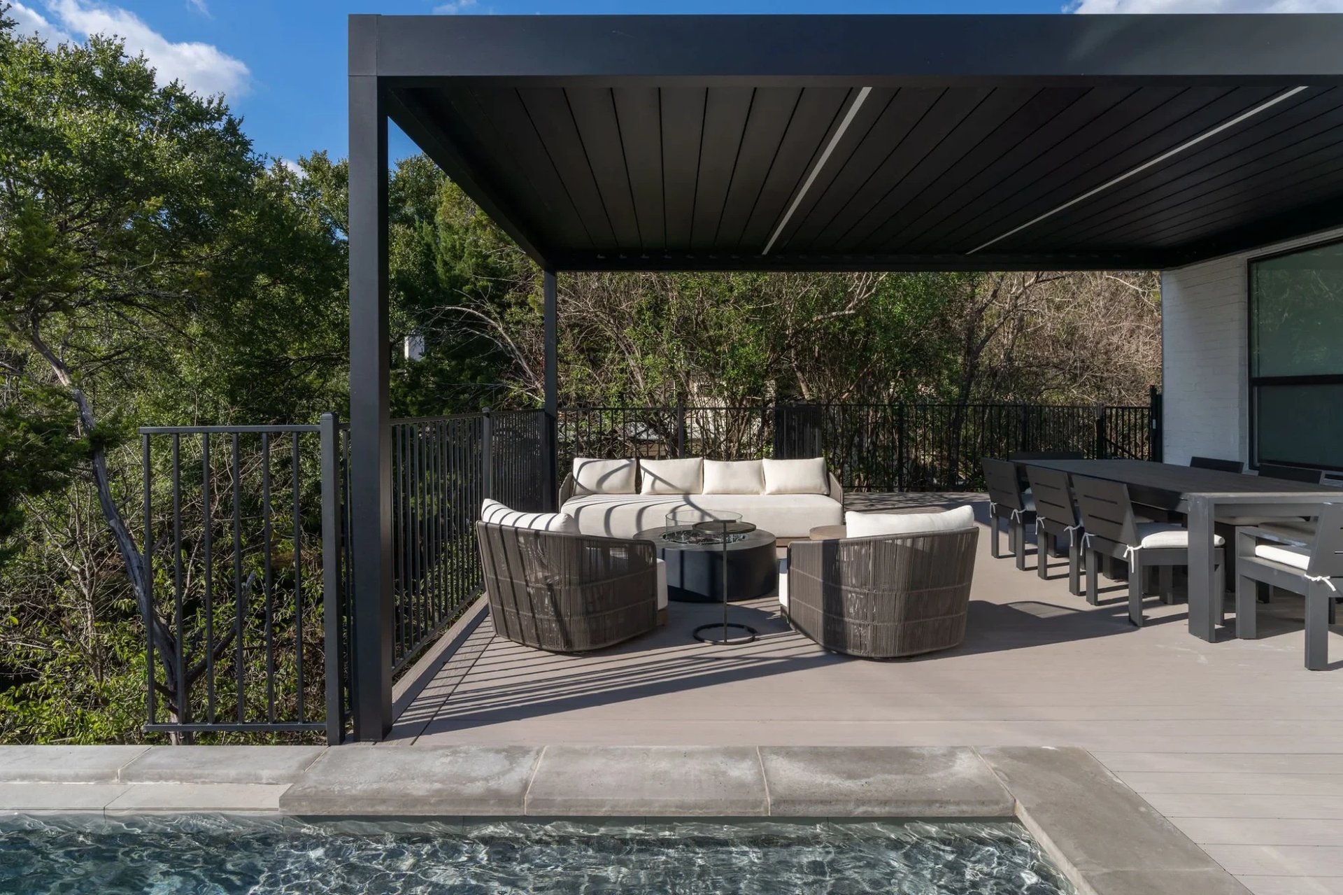 Deck with a black pergola and wicker seating beside an infinity pool over the Hill Country