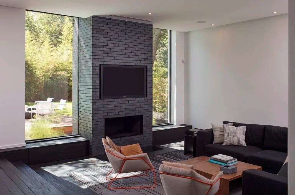 Living room with a gray brick fireplace and mounted TV, dark sectional, and tall windows to the yard