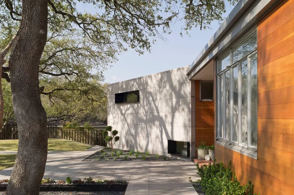 White and warm-wood modern home with a recessed window, live oaks and a stone path on the approach