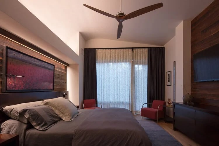 Bedroom with a wood-paneled accent wall, abstract art over the bed and a sculptural ceiling fan