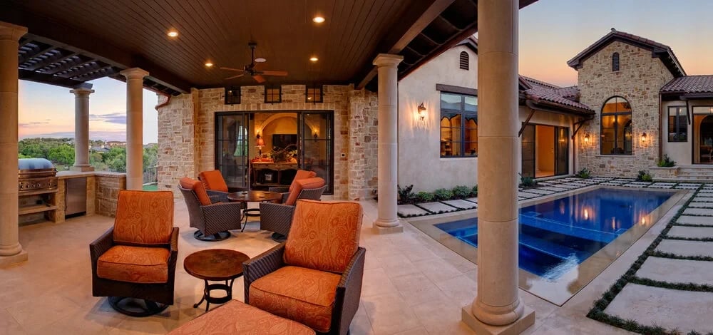 Covered patio with orange chairs and stone columns overlooking a geometric courtyard pool at sunset