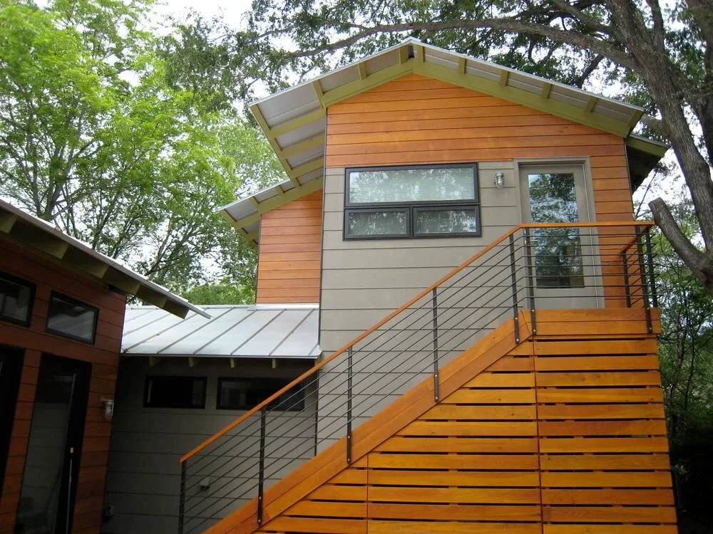 Cedar-clad modern home with a metal roof and exterior stairway with wood-and-cable railing among trees