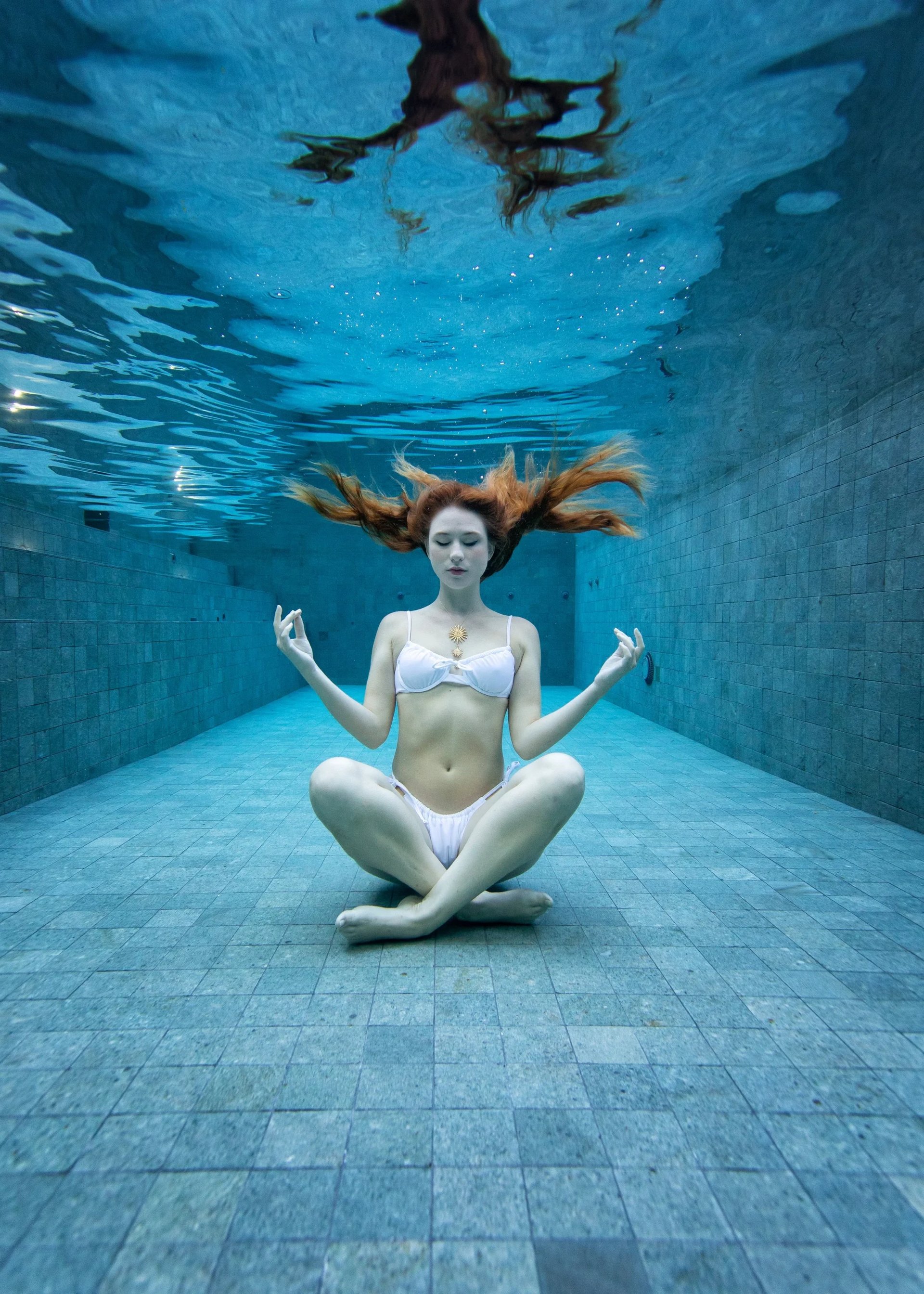 Underwater view of a swimmer trailing bubbles as she dives across the floor of a tiled pool