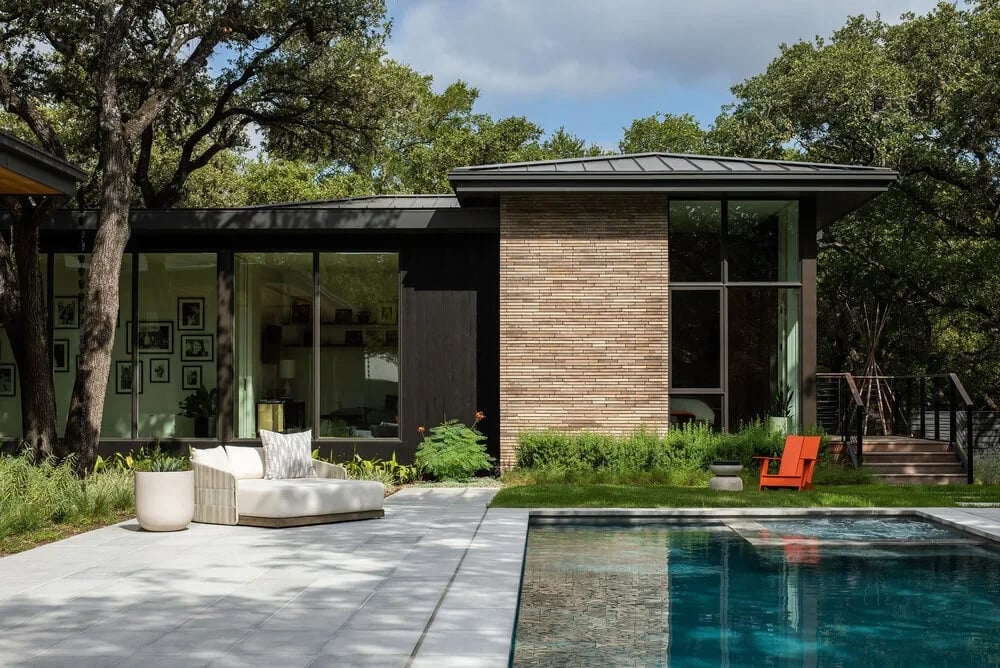 Geometric pool with stone coping reflecting a glass-walled modern home and surrounding live oaks