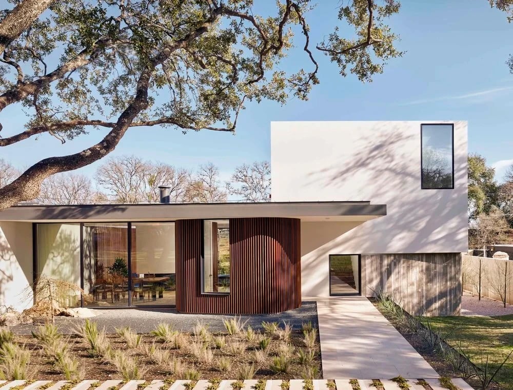 Two-story modern home with wood and white walls and a curved entry framed by a large oak