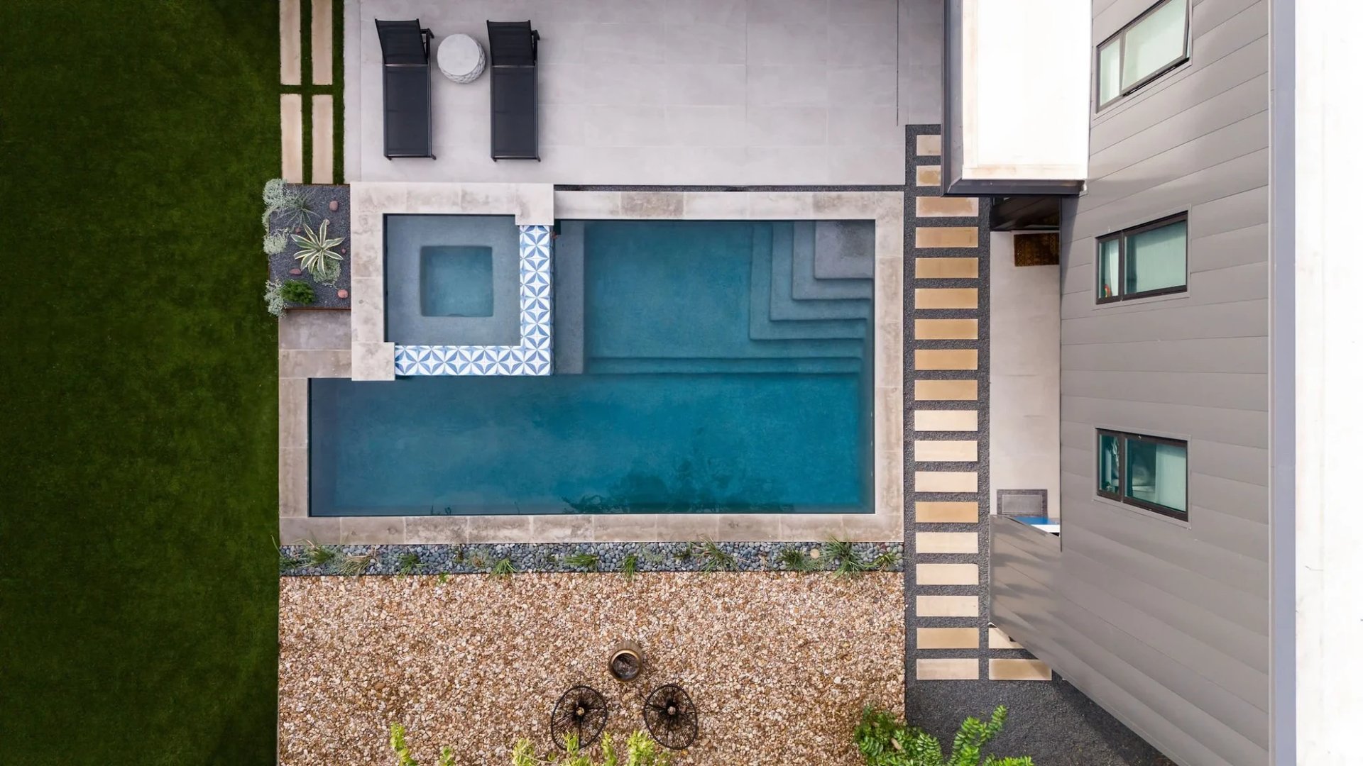 Aerial of a geometric pool with a square spa and patterned blue tile beside a modern home