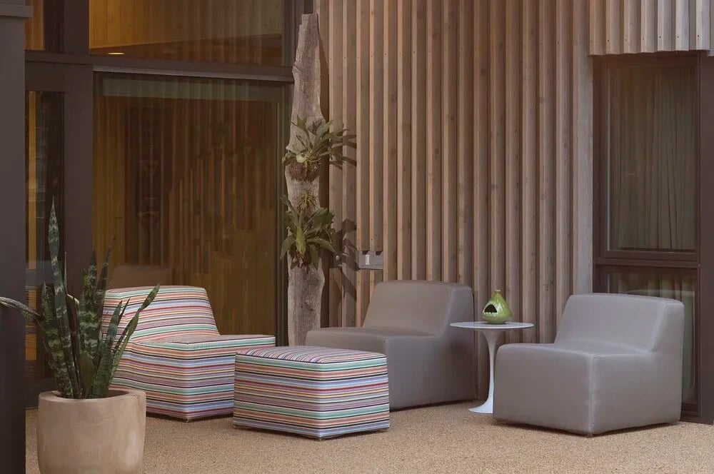 Cedar-slat courtyard wall with striped modern lounge chairs, an ottoman and a potted snake plant