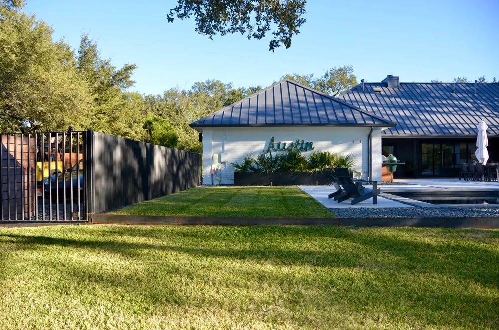 Metal-roof home behind a dark fence and wide lawn with scattered oaks at golden hour