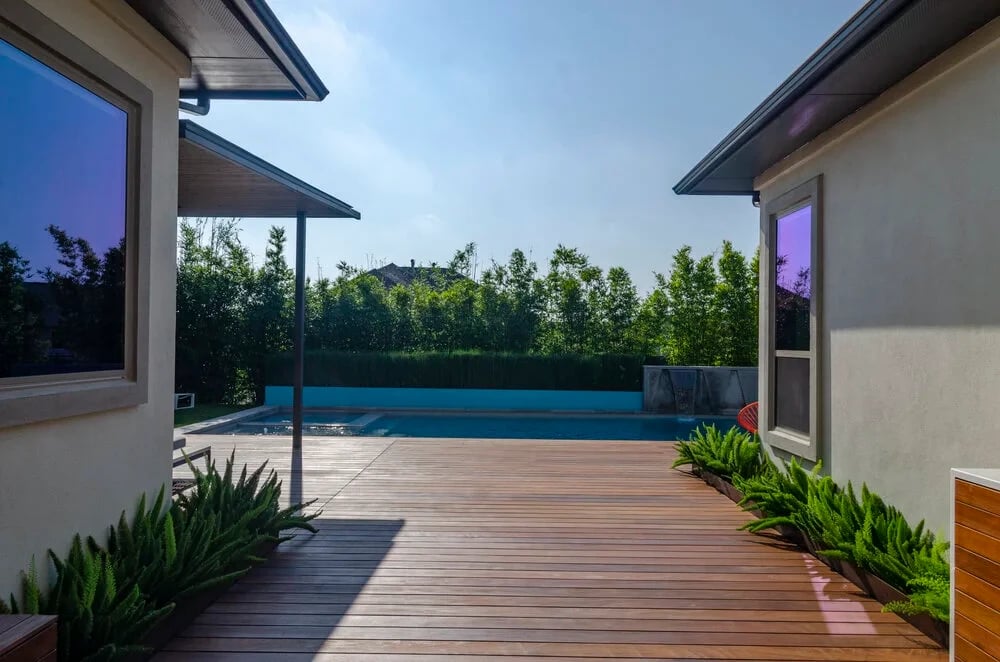 View between two homes across an ipe deck to a geometric pool with scuppers and a bamboo hedge