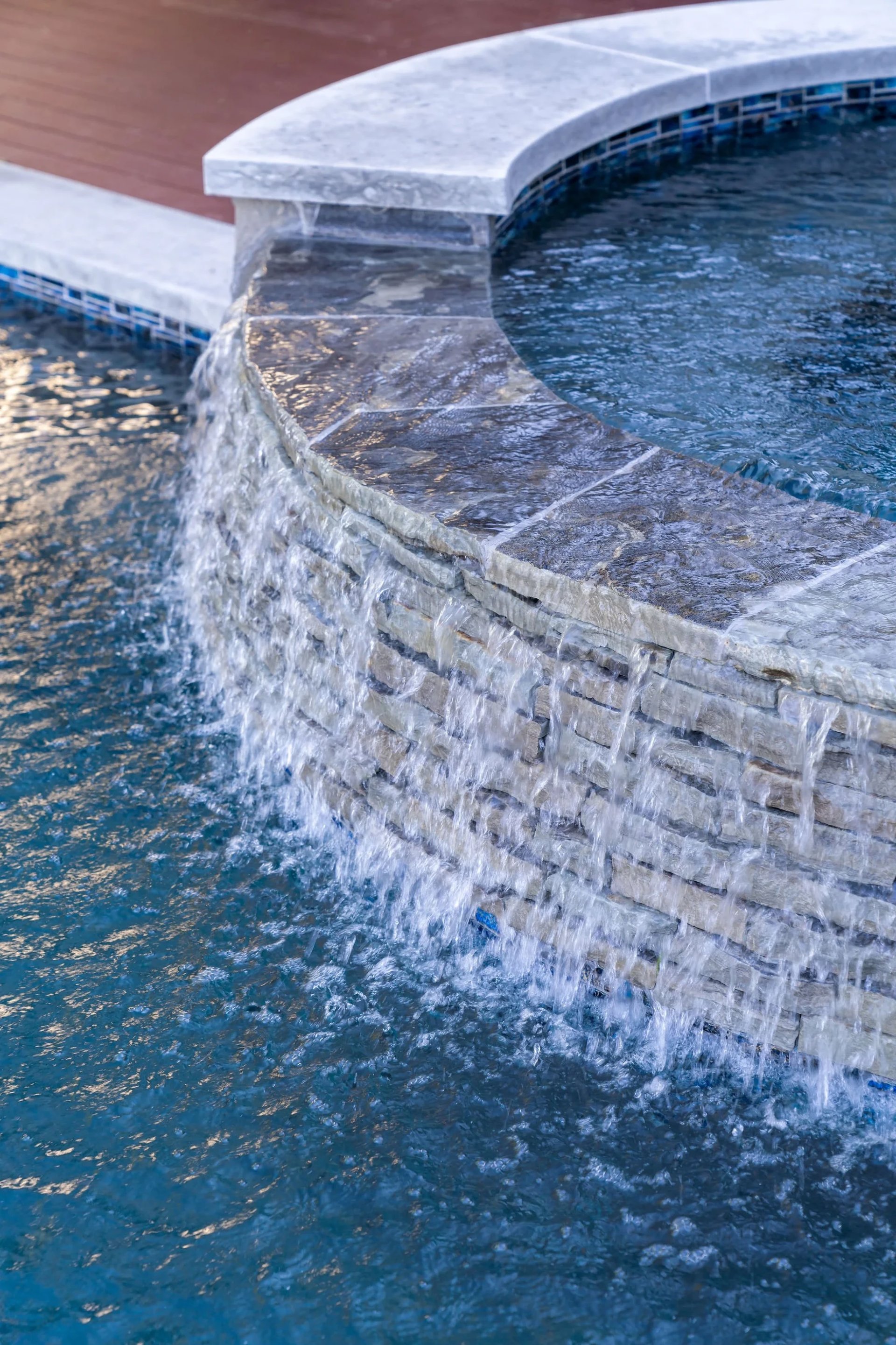 Travertine spa wall with a sheet waterfall cascading over stone into the pool below, close detail view