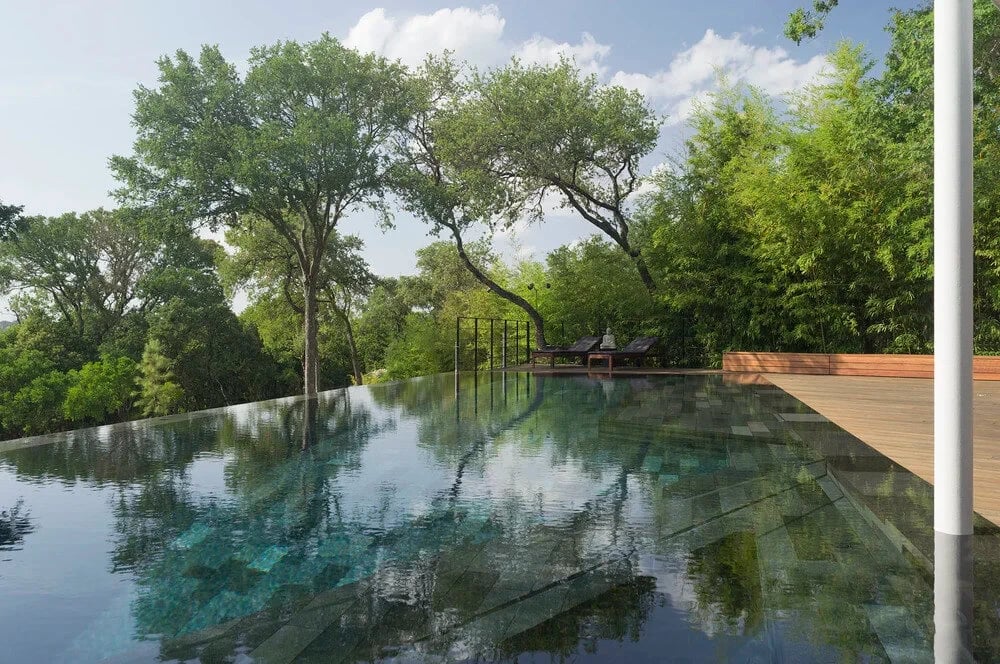 Infinity pool with a teal tiled bottom reflecting live oaks, its edge dropping toward the treetops