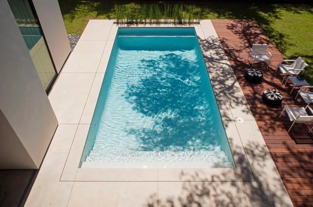 Overhead view of a rectangular geometric pool with limestone coping, reeds, and an adjacent wood deck
