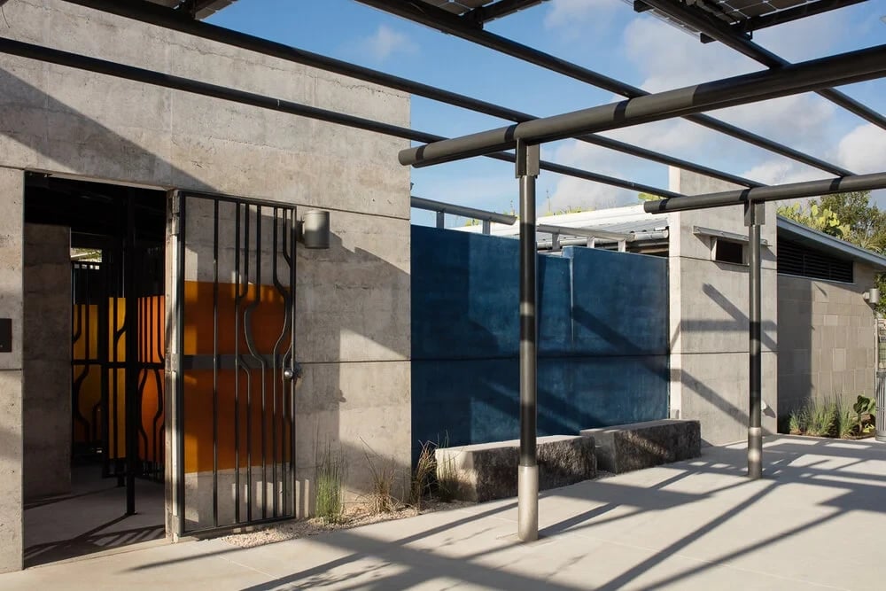Long blue-and-concrete trough sink in a courtyard, with a tree and orange gate beyond