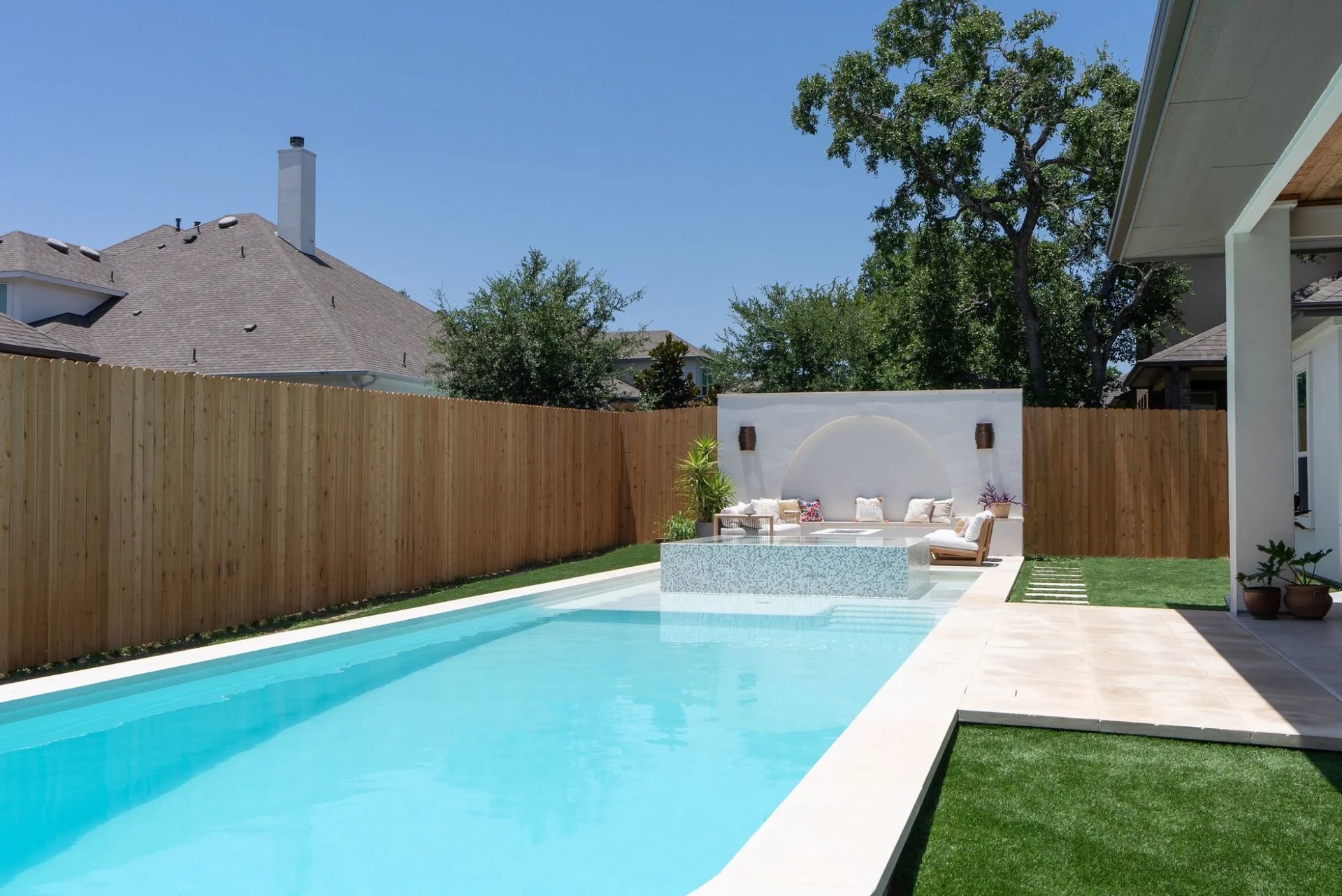 Geometric pool with a raised glass-tile spa, a stucco feature wall and lounge seating along a limestone deck
