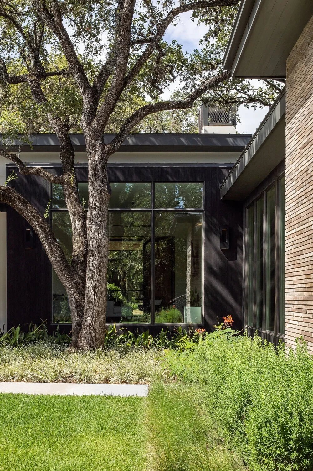 Modern home with stone and dark cladding beside a geometric pool, lounge seating on a paver patio