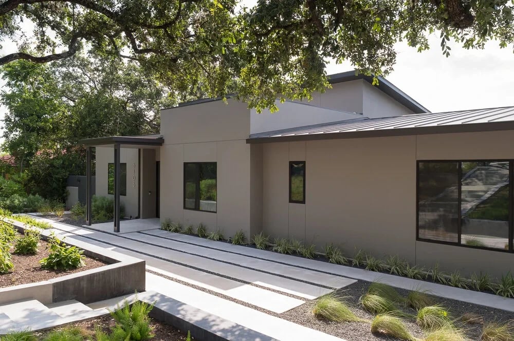 Single-story modern stucco home with clerestory windows and a planted entry walkway shaded by a live oak