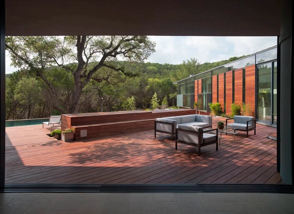 Wood deck with patio furniture viewed from inside, looking out to oaks and Hill Country slopes