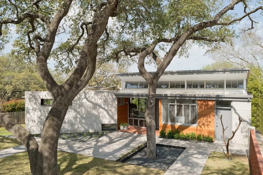 Two-story modern home in white stone and cedar siding, framed by live oaks and a lawn