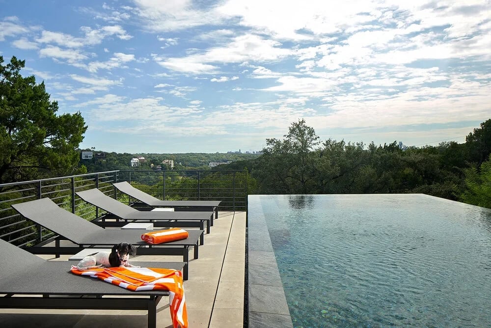 Infinity pool with lounge chairs overlooking the West Lake Hills under a cloudy sky