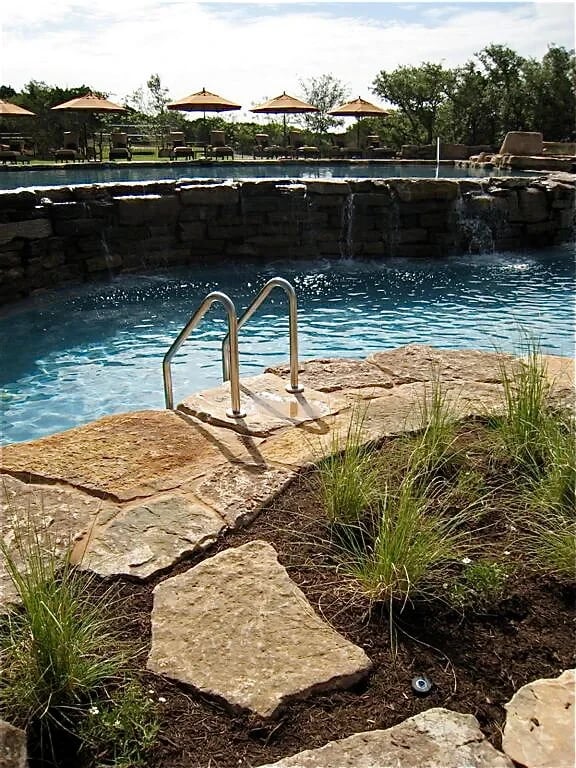 Freeform pool with stairs into the water and stone steps up through grasses and boulders