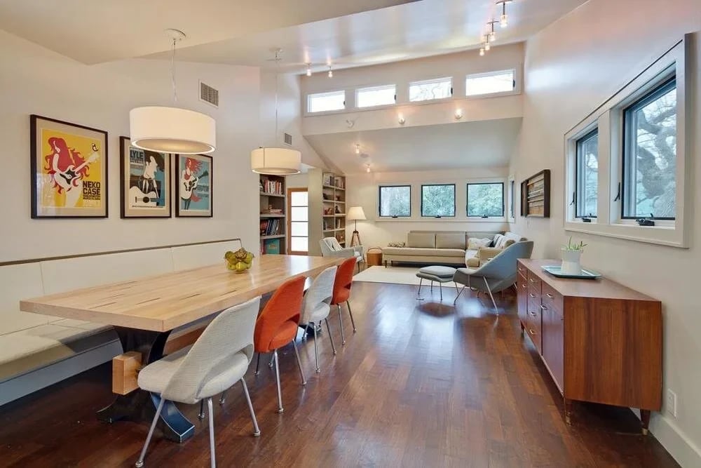 Open dining and living area with wood floors, music posters and a long maple table beside a built-in bench