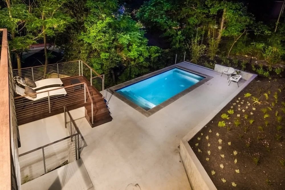 Small gunite pool lit at dusk on a terraced concrete deck with lounge chairs and a hillside backdrop