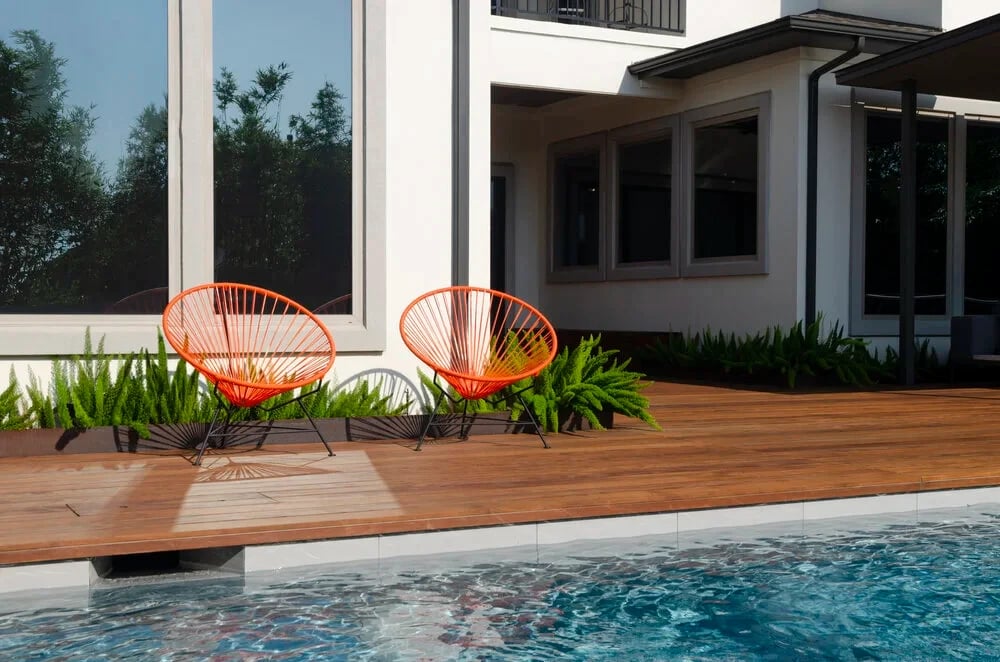 Orange string chairs on an ipe deck at the edge of a geometric pool beside a modern home