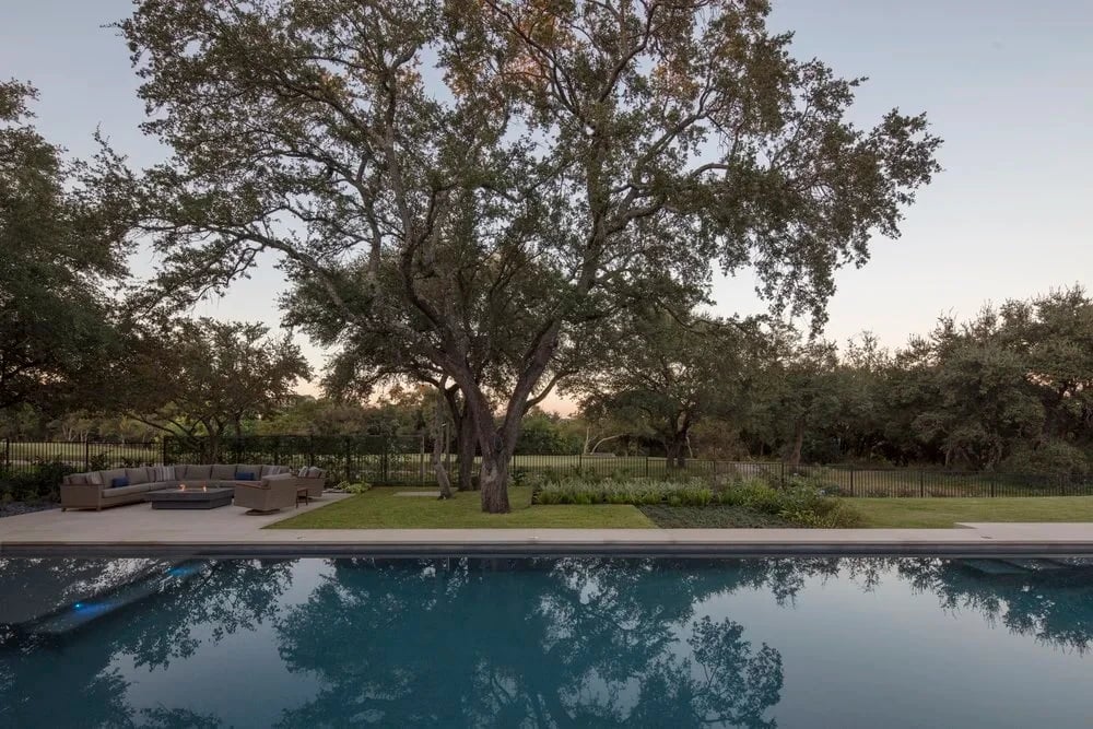 Geometric pool reflecting a broad oak and dusk sky, surrounded by lawn in Barton Creek