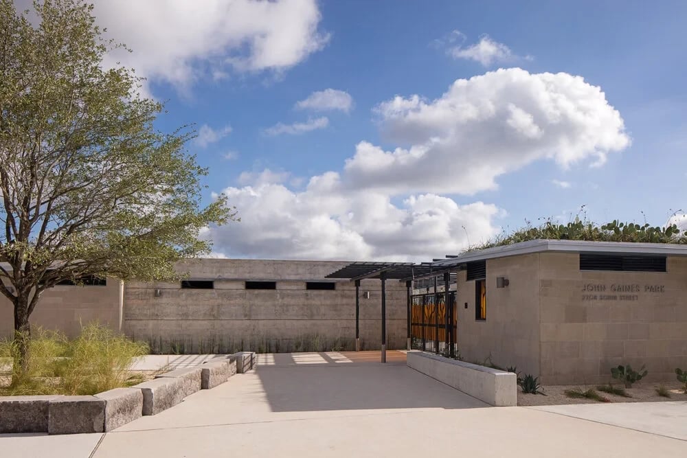 Concrete-walled park bathhouse with a steel pergola and orange gate under a cloudy blue sky