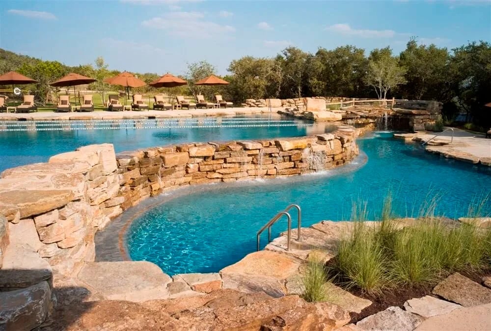 Freeform pool with stone waterfalls and boulders framed by trees in Spanish Oaks