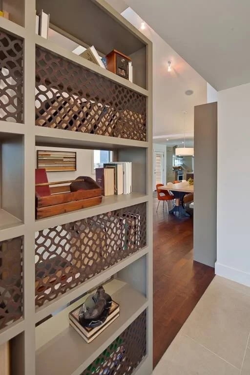 Hallway view past a perforated metal-paneled bookshelf toward a wood-floored dining room