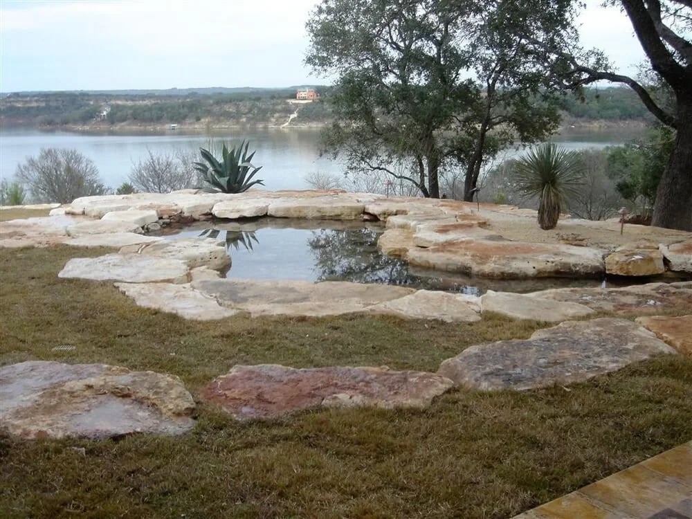 Natural stone spa edged in limestone overlooking a lake and wooded hills in the Hill Country
