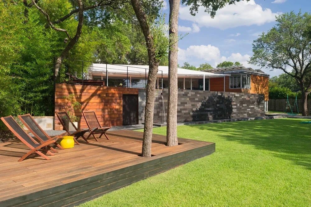 Cedar-and-stone modern home with a wood deck, lounge chairs and a green lawn under blue sky